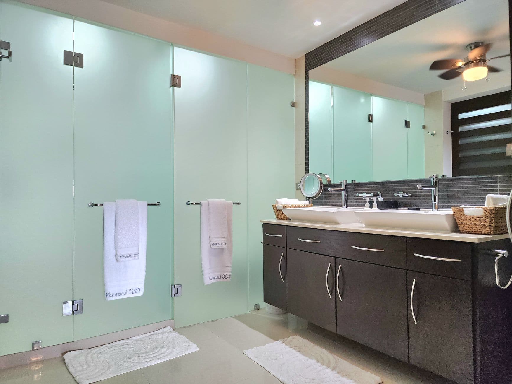 Badkamer met matglazen wanden, handdoeken aan twee stangen en een wastafelmeubel met twee wasbakken