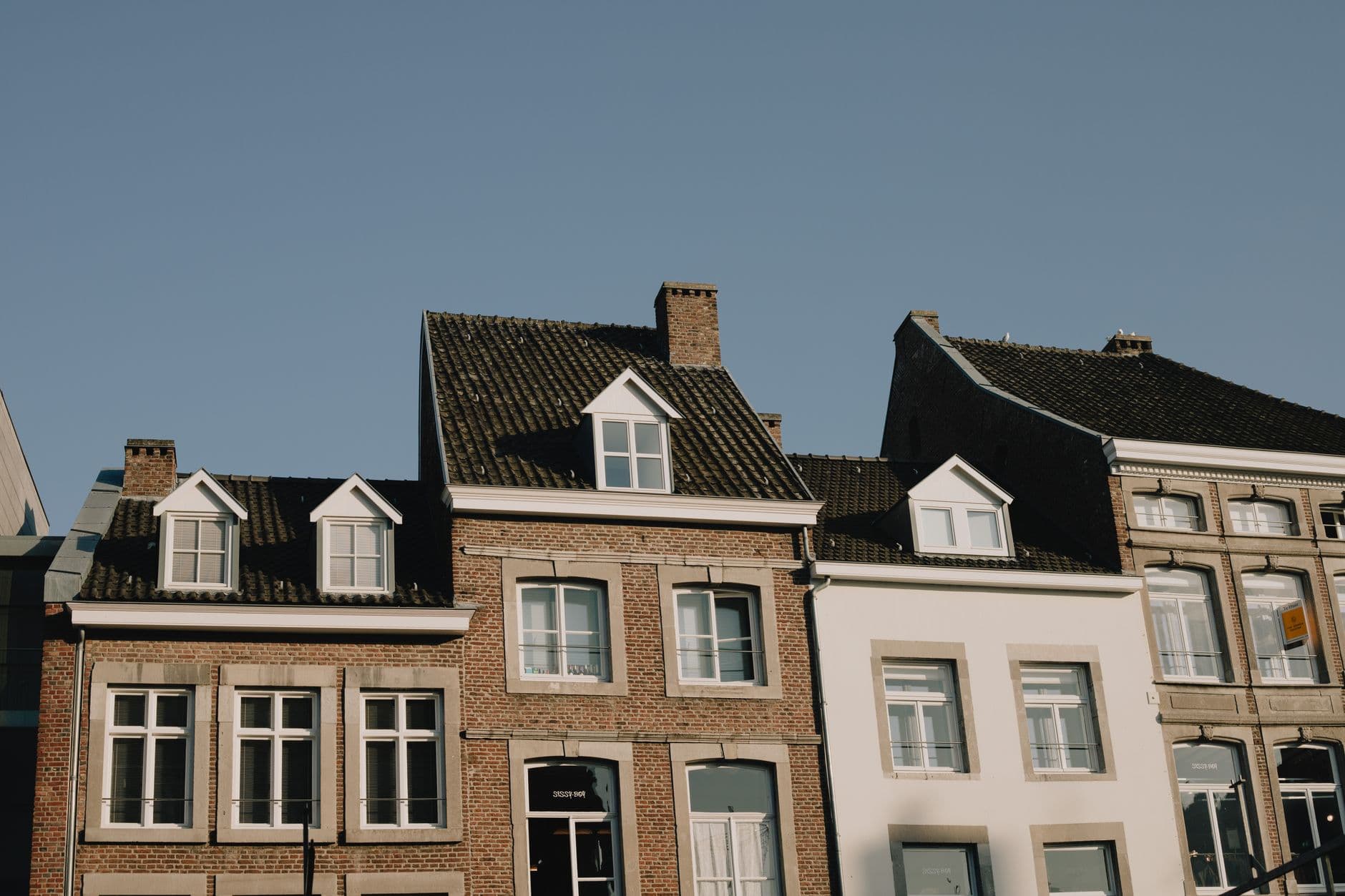 Oude rijhuizen met dakkapellen en bakstenen en witte gevels tegen een blauwe lucht