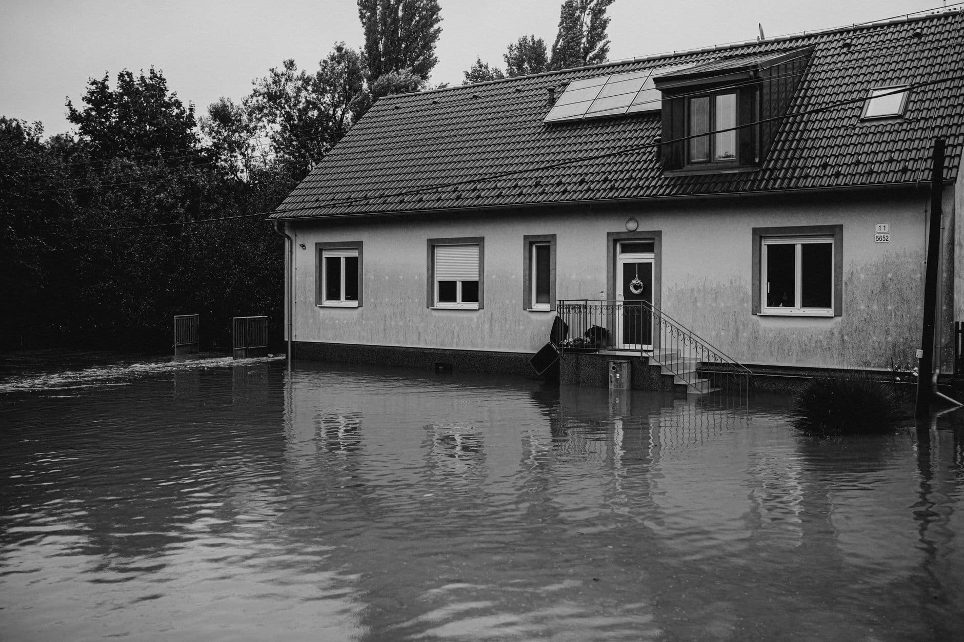 Huis in zwart-wit met overstromingswater tot tegen de gevel en de trap naar de voordeur