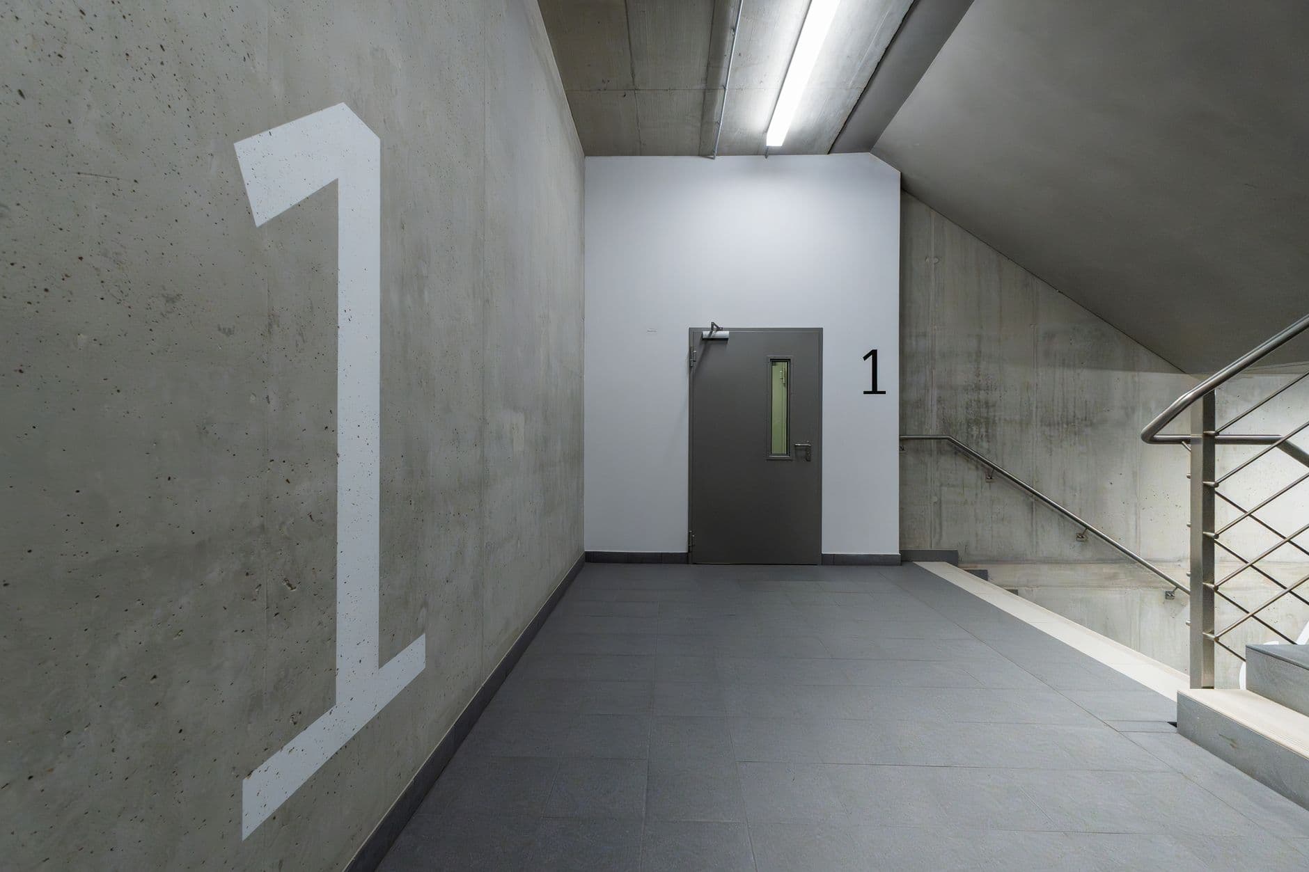 Betonnen trappenhal met een groot cijfer 1 op de muur, een grijze deur en een trap