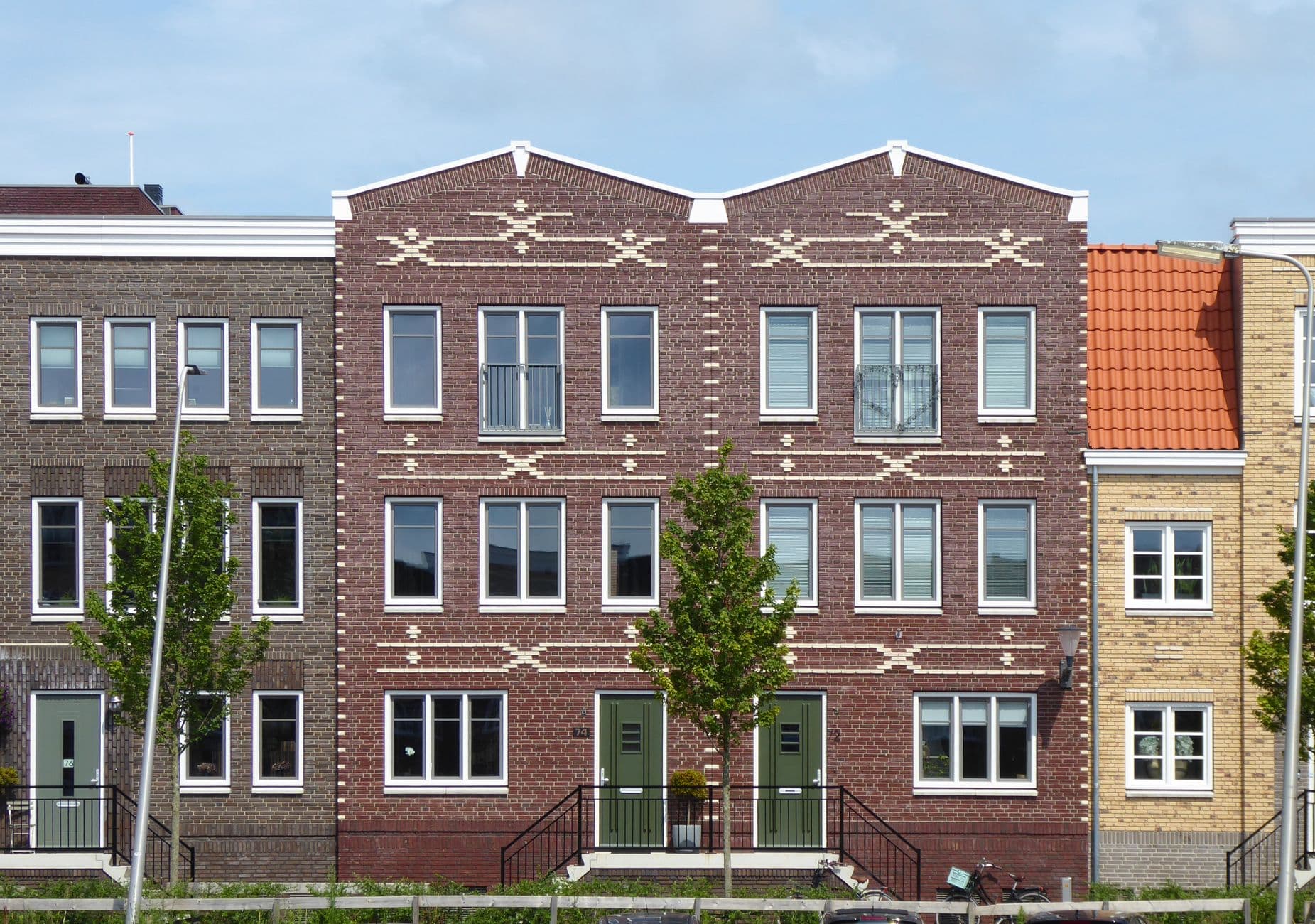 Rij nieuwe bakstenen huizen met decoratief metselwerk en jonge bomen
