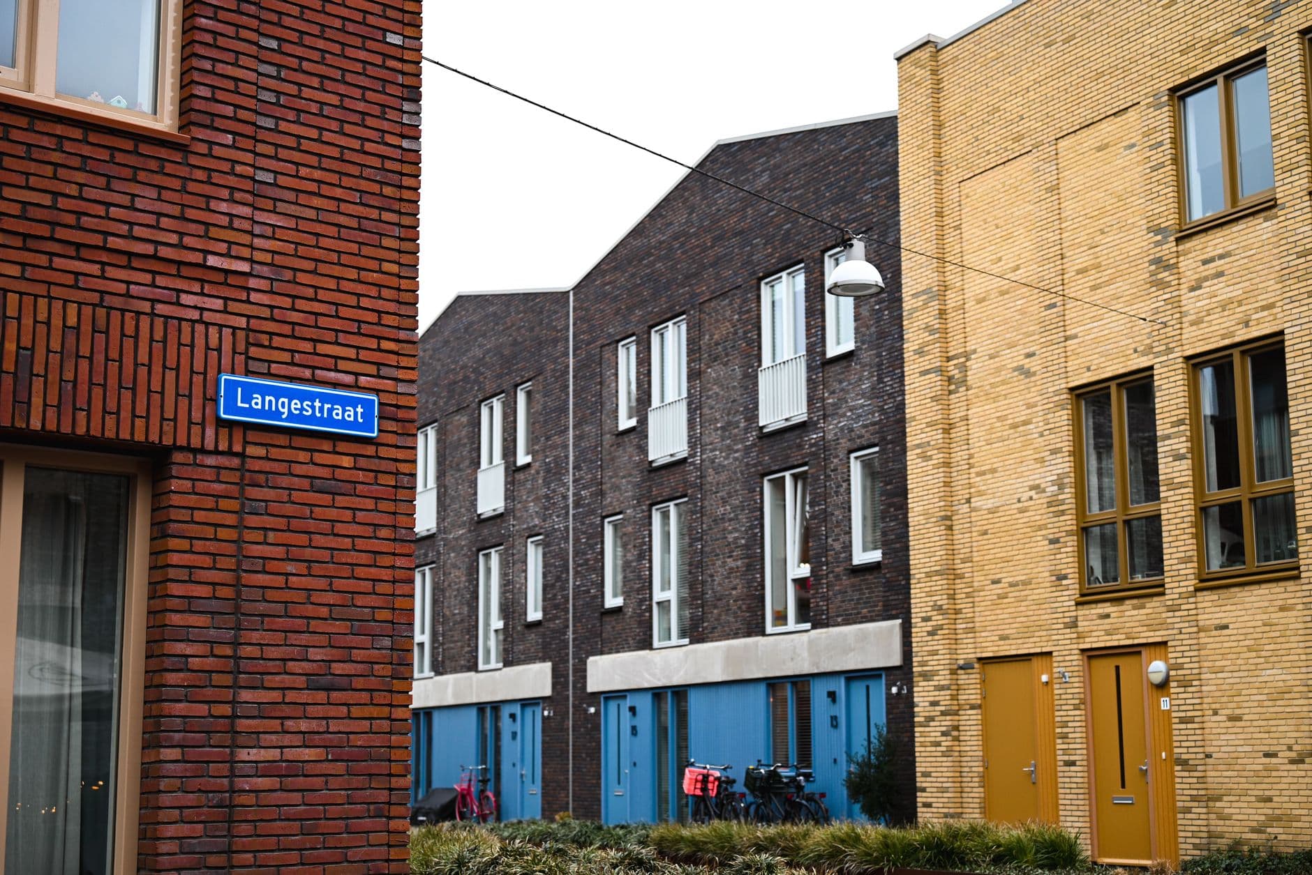 Bakstenen en gele woningen aan een straat met een blauw straatnaambord