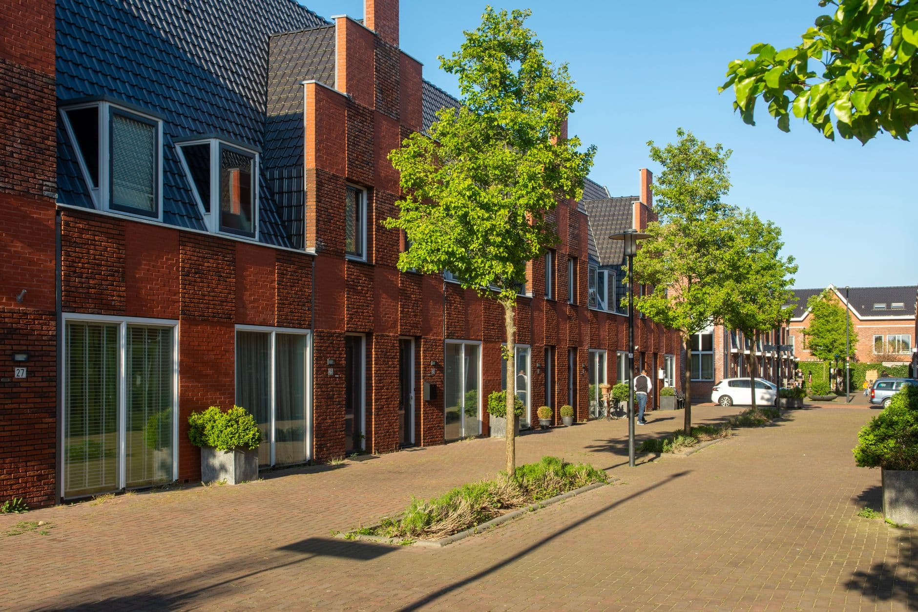 Nieuwe bakstenen rijwoningen aan een geklinkerde straat met bomen