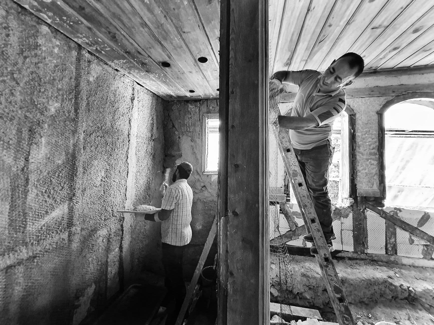 Twee mannen die een kamer met een houten plafond renoveren, in zwart-wit