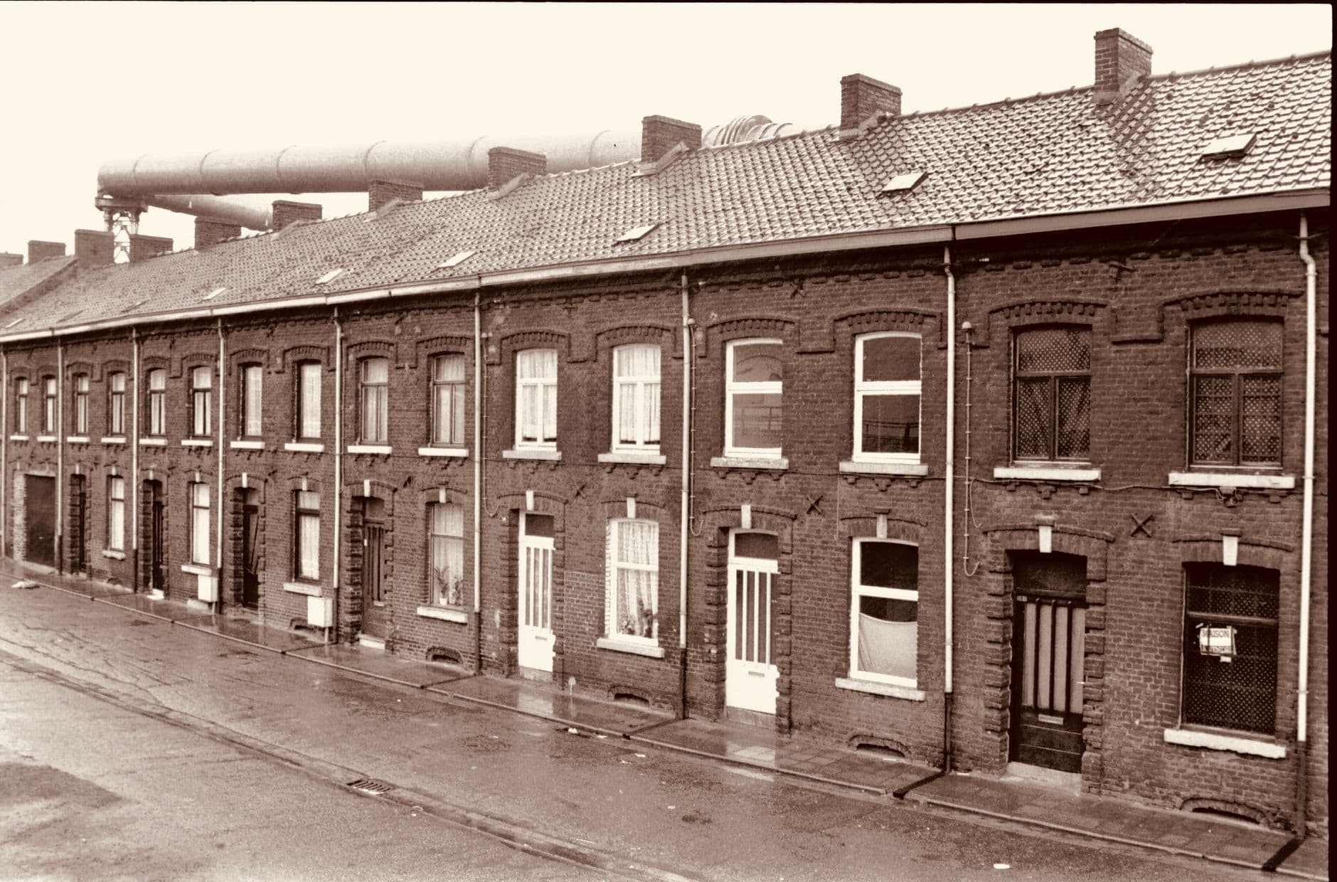 Rij arbeiderswoningen in baksteen langs een natte straat