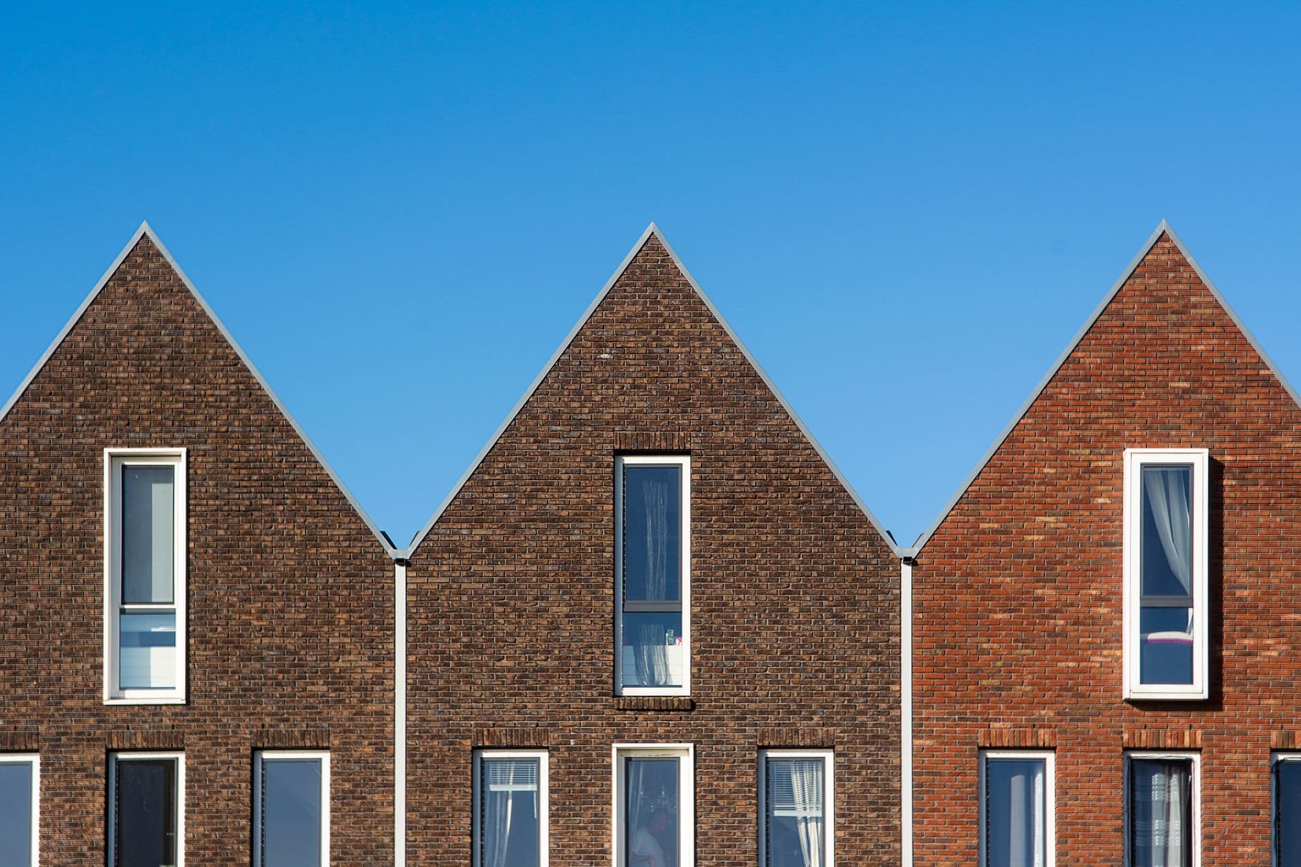 Drie bakstenen woningen met puntgevels tegen een blauwe lucht
